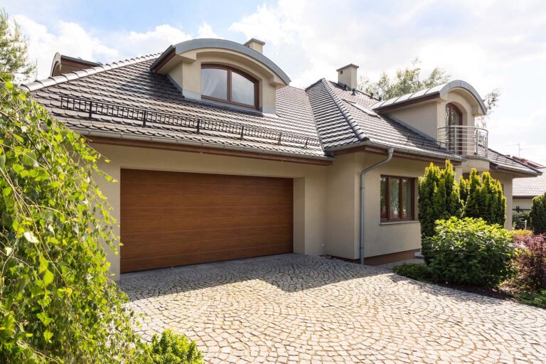 Detached family house exterior with cobblestone driveway to the garage and spruce garden
