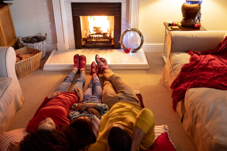 Front view of a mixed race couple with their young daughter in their sitting room at Christmas, lying on the floor by a fireplace and embracing