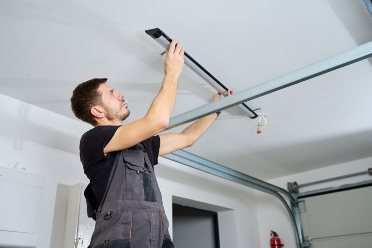 Man in workwear installing a linear LED light fixture on the ceiling indoors. Concept of electrical installation, maintenance work and home renovation.
