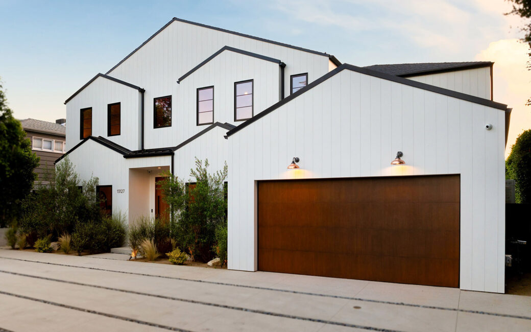Modern white house with a wooden garage door and landscaped garden under a clear sky.
