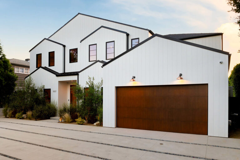 Modern white house with a wooden garage door and landscaped garden under a clear sky.